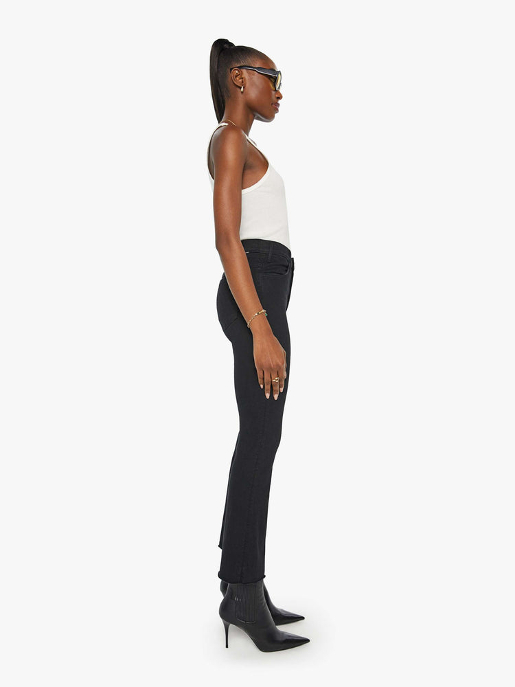 Side view of a womens black jean featuring a high rise, a flare leg, and an ankle length raw hem.