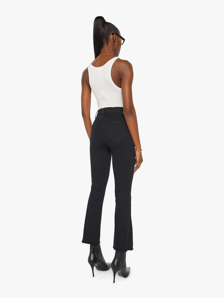 Back view of a womens black jean featuring a high rise, a flare leg, and an ankle length raw hem.