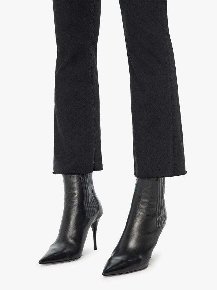 Front 3/4 close up view of a womens black jean featuring a high rise, a flare leg, and an ankle length raw hem.