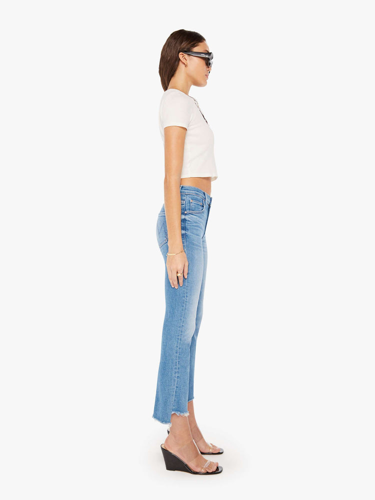 Side view of a woman in a mid blue high-waisted bootcut is cropped at the ankle with a frayed step-hem.