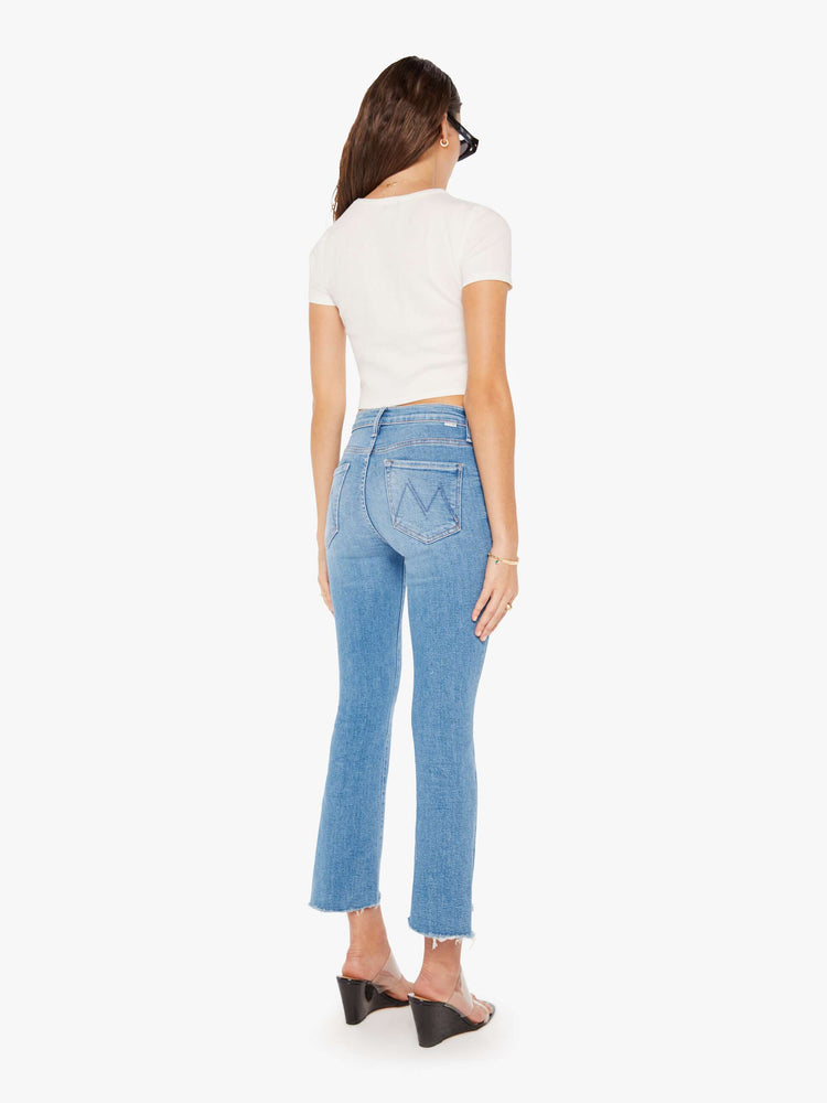 Back view of a woman in a mid blue high-waisted bootcut is cropped at the ankle with a frayed step-hem.