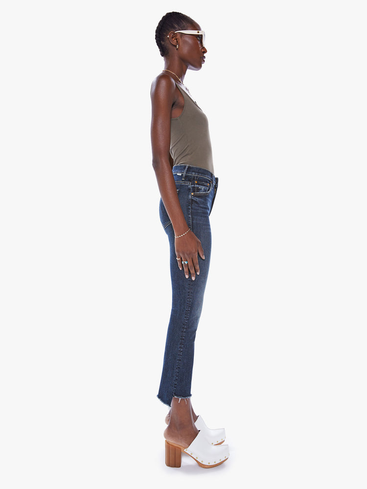 Side view of a womens dark denim wash jean featuring a high rise and a bootcut step fray.