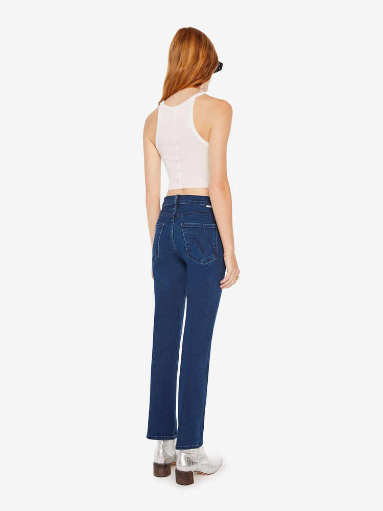 Back view of a woman high-rise flare with a button fly and a clean ankle-length hem in a dark blue wash.