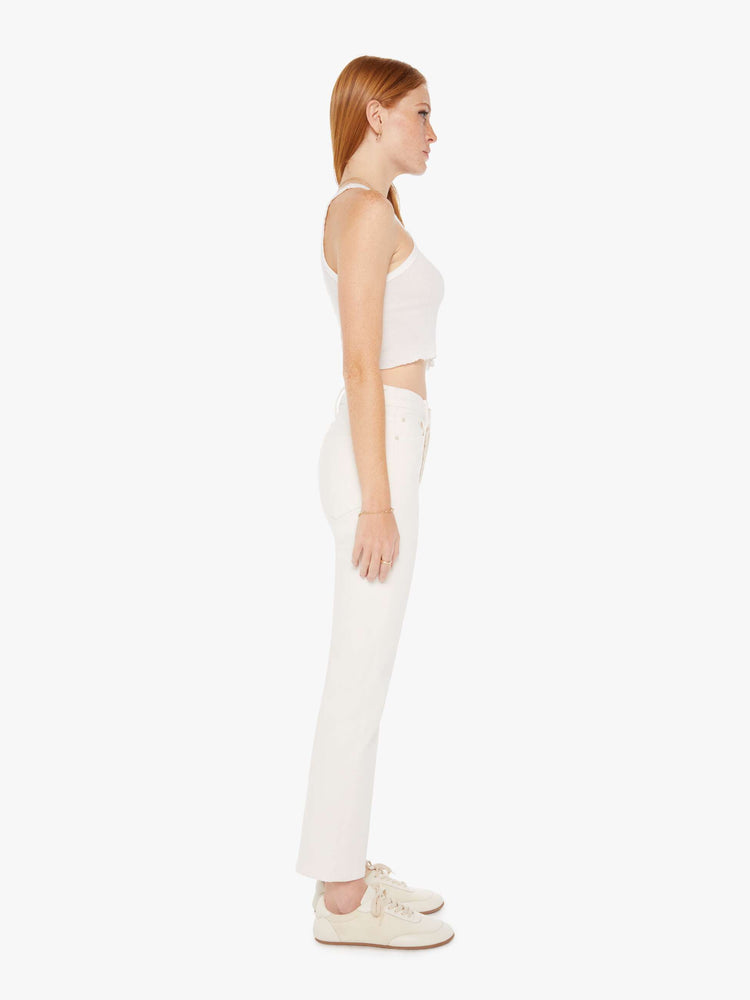 Side view of an off white color jean featuring a high rise and an ankle length flare with clean hem.