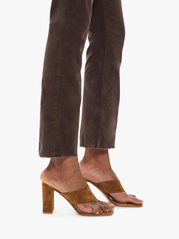 Side close up view of a womens brown corduroy pant featuring a high rise and a raw cut flare hem.