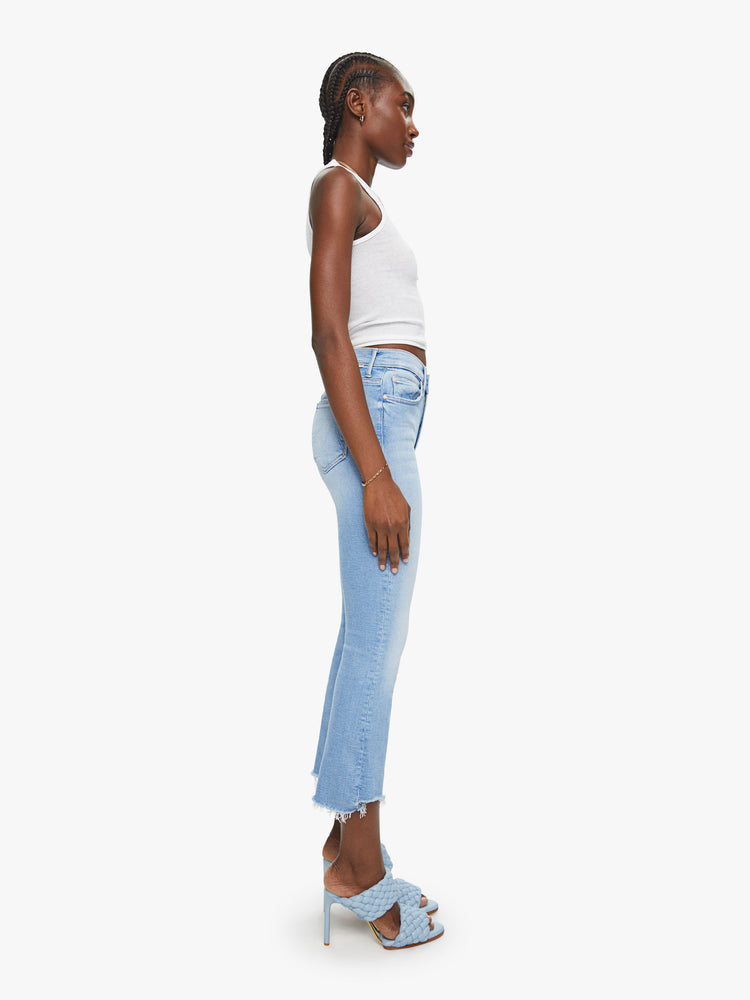 Side view of a womens light blue jean featuring a high rise, bootcut, and a crop step frayed hem.