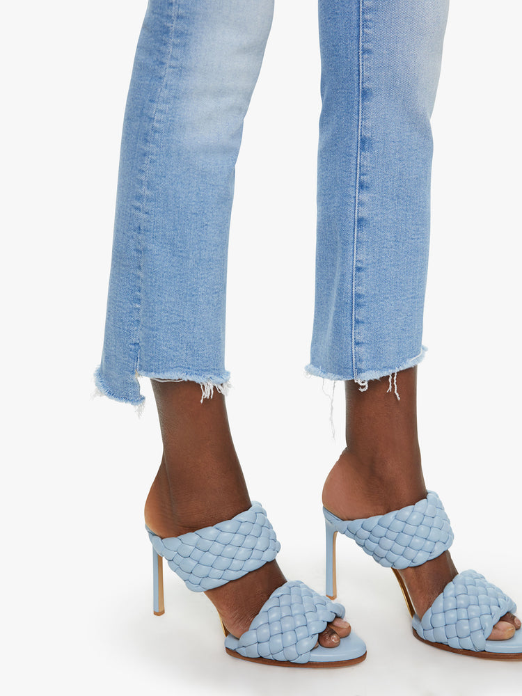 Side close up view of a womens light blue jean featuring a bootcut, and a crop step frayed hem.