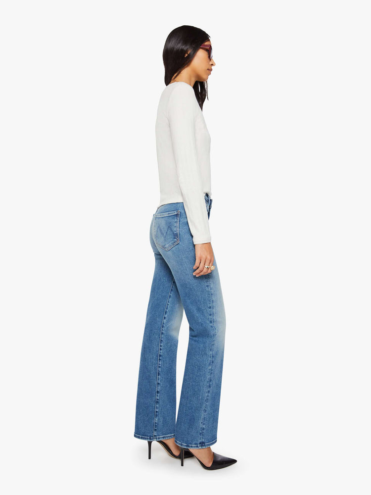 Side view of a woman in a mid blue high-rise straight leg jean with a 32-inch inseam and a clean hem.