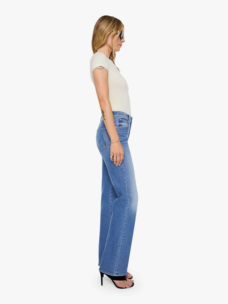 Side view of a woman in mid blue high-rise straight leg jean with a 32-inch inseam and a clean hem.