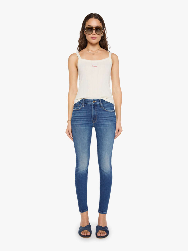 Front view of a woman in a mid blue skinny jean has a high rise with a zip fly, 29-inch inseam and a clean hem.