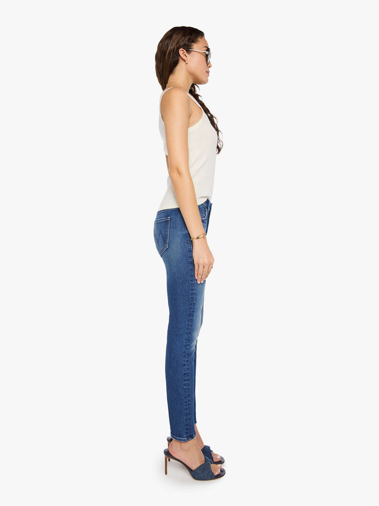 Side view of a woman in a mid blue skinny jean has a high rise with a zip fly, 29-inch inseam and a clean hem.