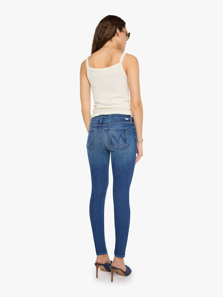 Back view of a woman in a mid blue skinny jean has a high rise with a zip fly, 29-inch inseam and a clean hem.
