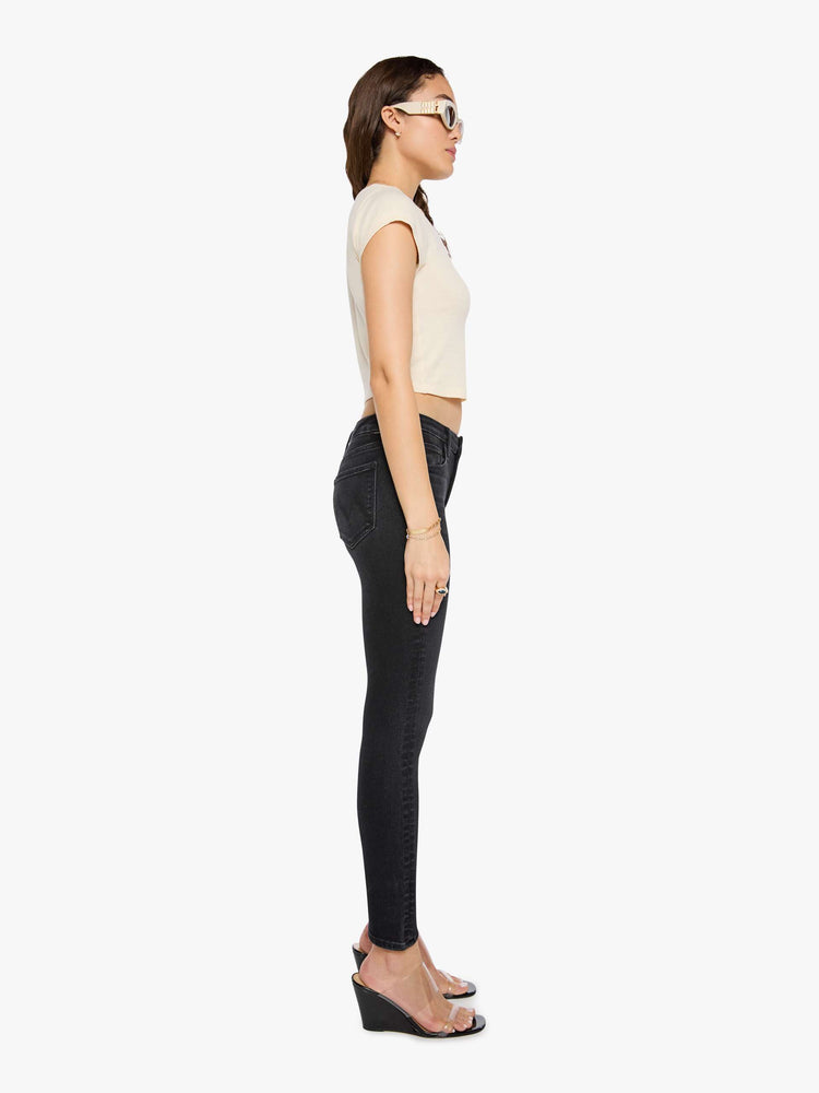 Side view of a woman in a black skinny has a mid rise with a zip fly, 29-inch inseam and a clean hem.
