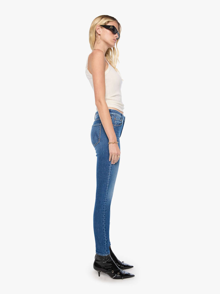 Side view of woman in a med blue skinny jean with a high rise with a zip fly, 30 3/4 inch inseam and a clean hem.