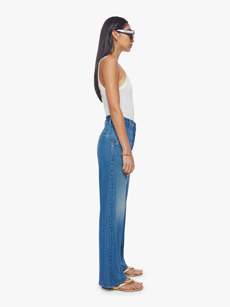 Side view of a woman super high-rise jeans with a loose wide leg, button fly, slit pockets and a 31-inch inseam with a clean hem in med-blue wash.