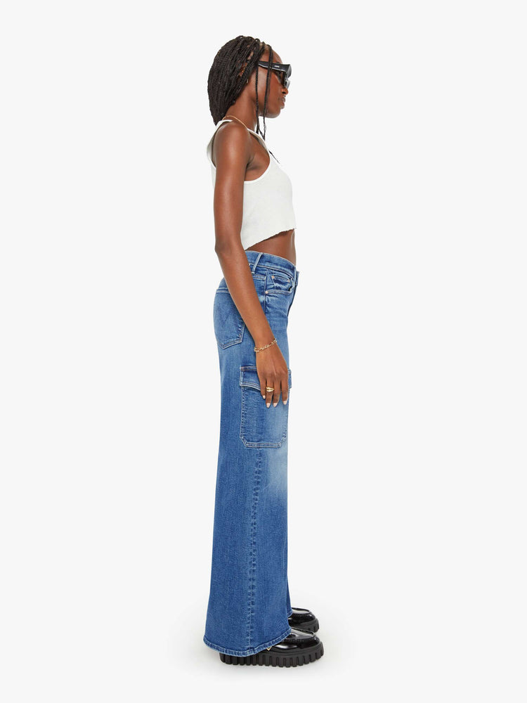 Side view of a woman med blue wide-leg cargo pants with a high rise, long 32-inch inseam and patch pockets on the thighs.