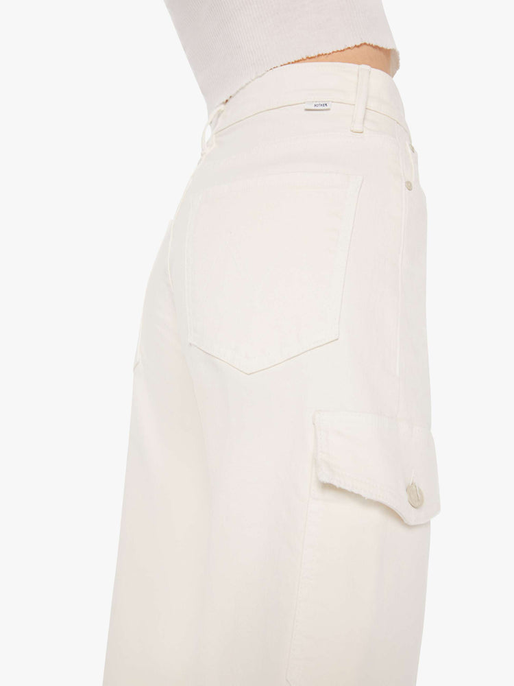 Side close up view of a woman wearing an off white jean featuring a high rise and cargo pockets, paired with a cropped white tank top.