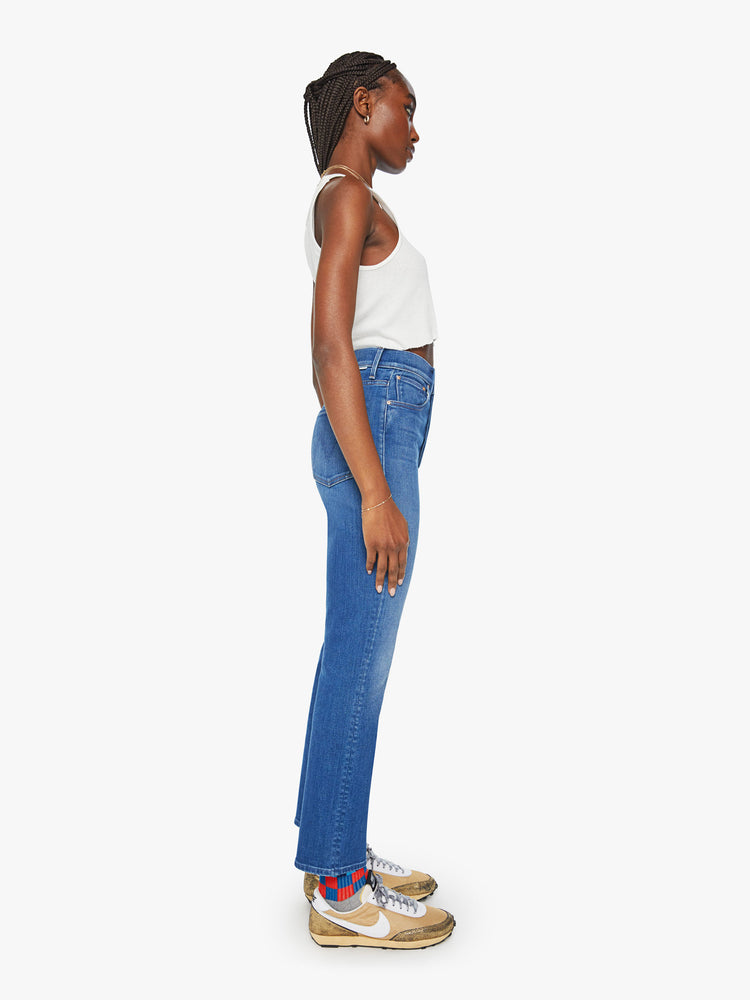 Side view of a woman slim straight leg with a button fly, low-set back pockets, high waist and a 29-inch inseam in mid blue wash.