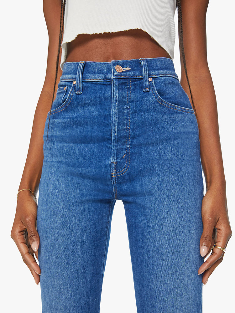 Waist close up view of a woman slim straight leg with a button fly, low-set back pockets, high waist and a 29-inch inseam in mid blue wash.