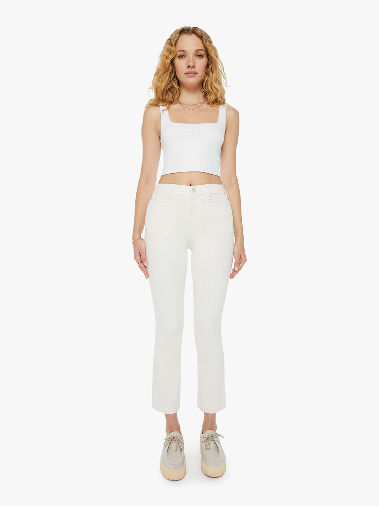 Front view of a woman in a high-rise ivory flare with patch pockets and a clean hem and tonal hardware. Paired with a white tank top and sneakers.