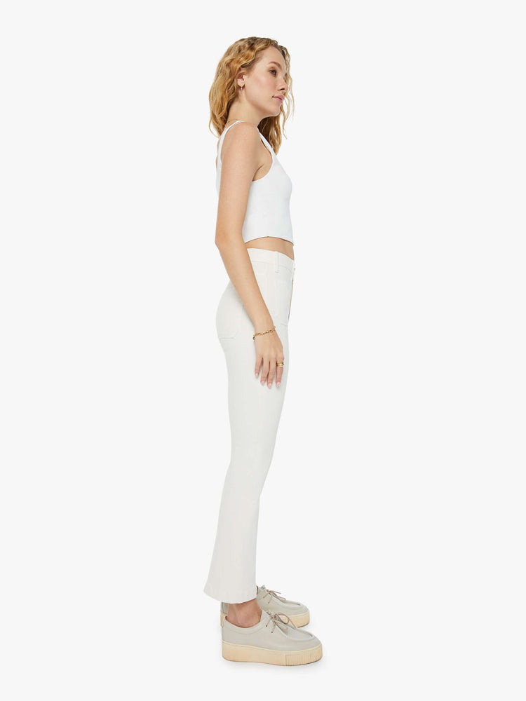 Side view of a woman in a high-rise ivory flare with patch pockets and a clean hem and tonal hardware. Paired with a white tank top and sneakers.
