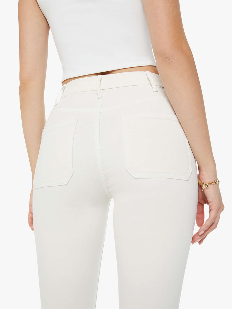 Swatch view of a woman in a high-rise ivory flare with patch pockets and a clean hem and tonal hardware. Paired with a white tank top.