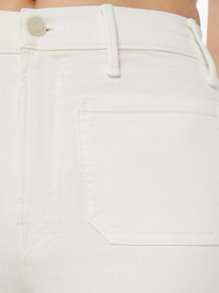 Detailed view of a woman in a high-rise ivory flare with patch pockets and a clean hem and tonal hardware.