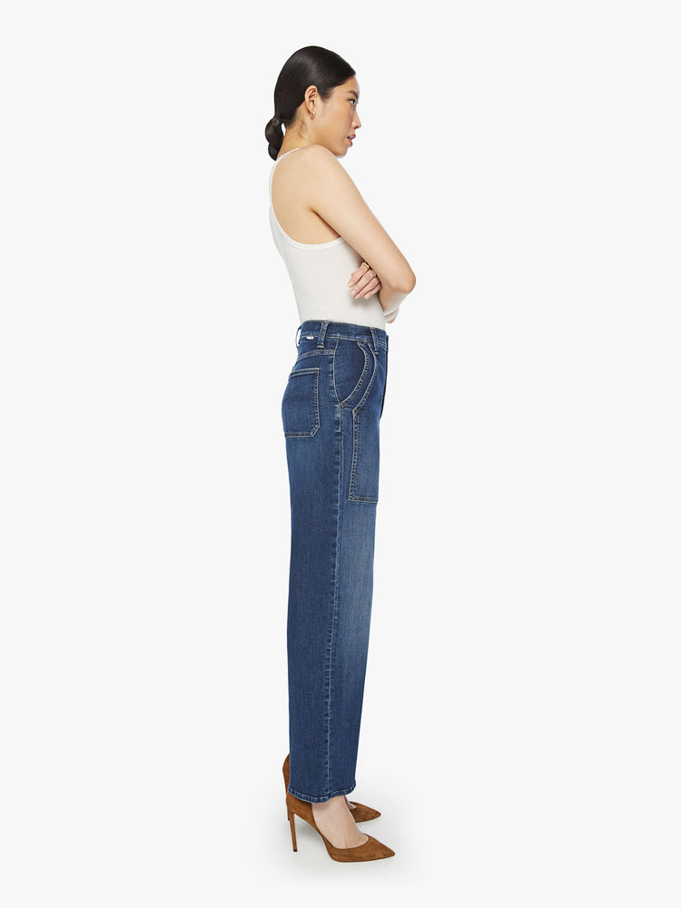 Side view of a woman wide straight-leg jeans with a super high rise, oversized double patch pockets and a clean hem in a dark blue wash.