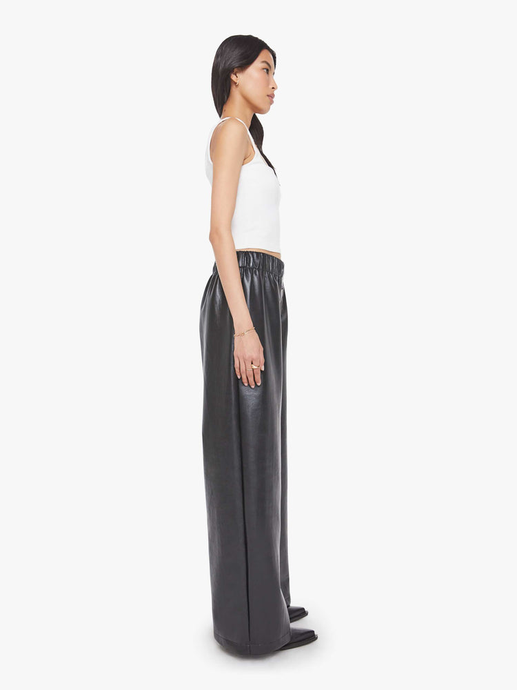 Side view of a woman in a black high-rise pants with an elastic waistband, loose wide leg, decorative exposed button-fly and a long 31-inch inseam. 