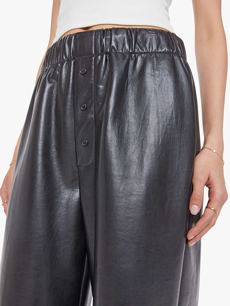 Close up view of a woman in a black high-rise pants with an elastic waistband, loose wide leg, decorative exposed button-fly and a long 31-inch inseam. 