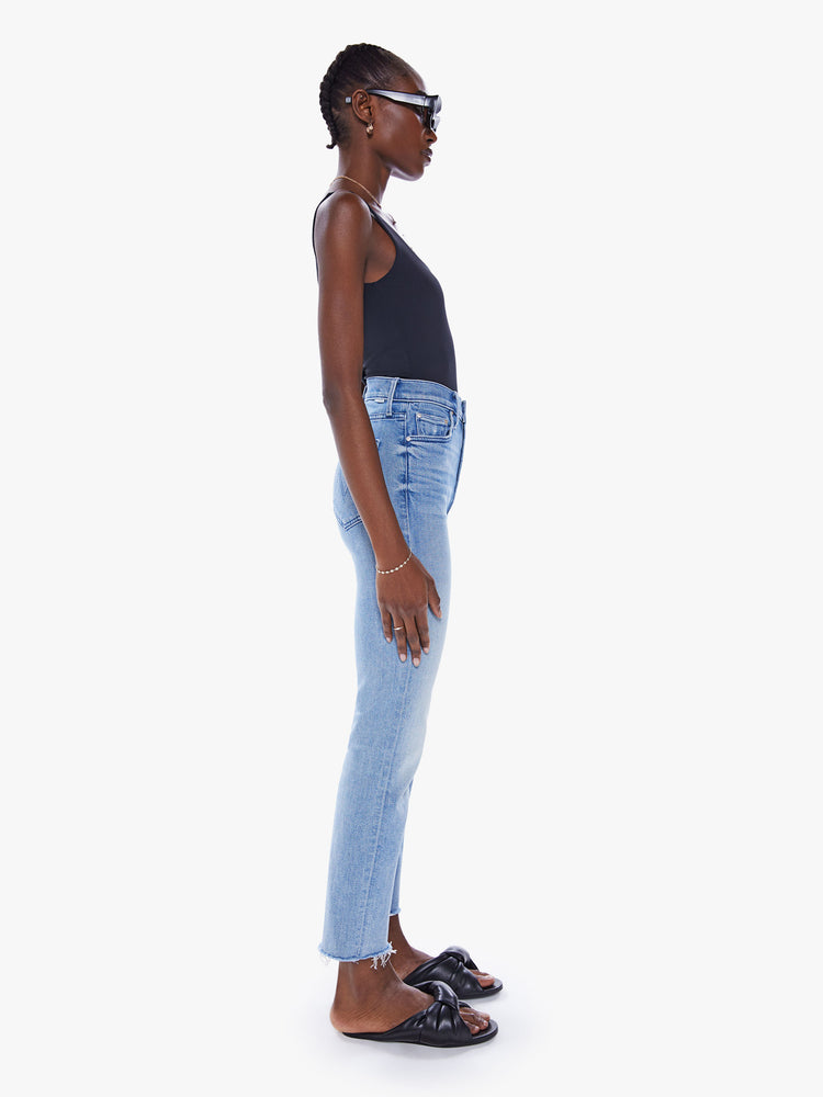 Side view of a woman high-waisted straight leg with an ankle-length inseam and a frayed hem in a light blue wash.