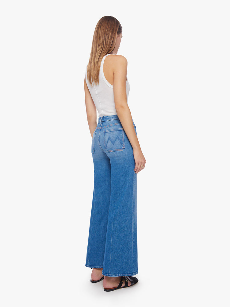 Back view of a woman mid-blue wash wide-leg jeans with a high rise, long inseam, patch pockets and a clean hem.