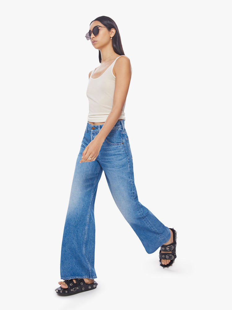 Walking view of a woman mid-rise wide leg jean with a button fly, slouchy, loose fit and a 30-inch inseam in a mid-blue wash.