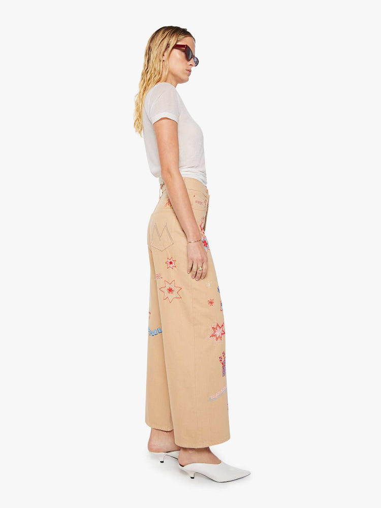 Side view of a woman in a khaki with colorful embroidery  wide-leg jeans are designed with a loose fit, button fly and a 30-inch inseam with a clean hem.  