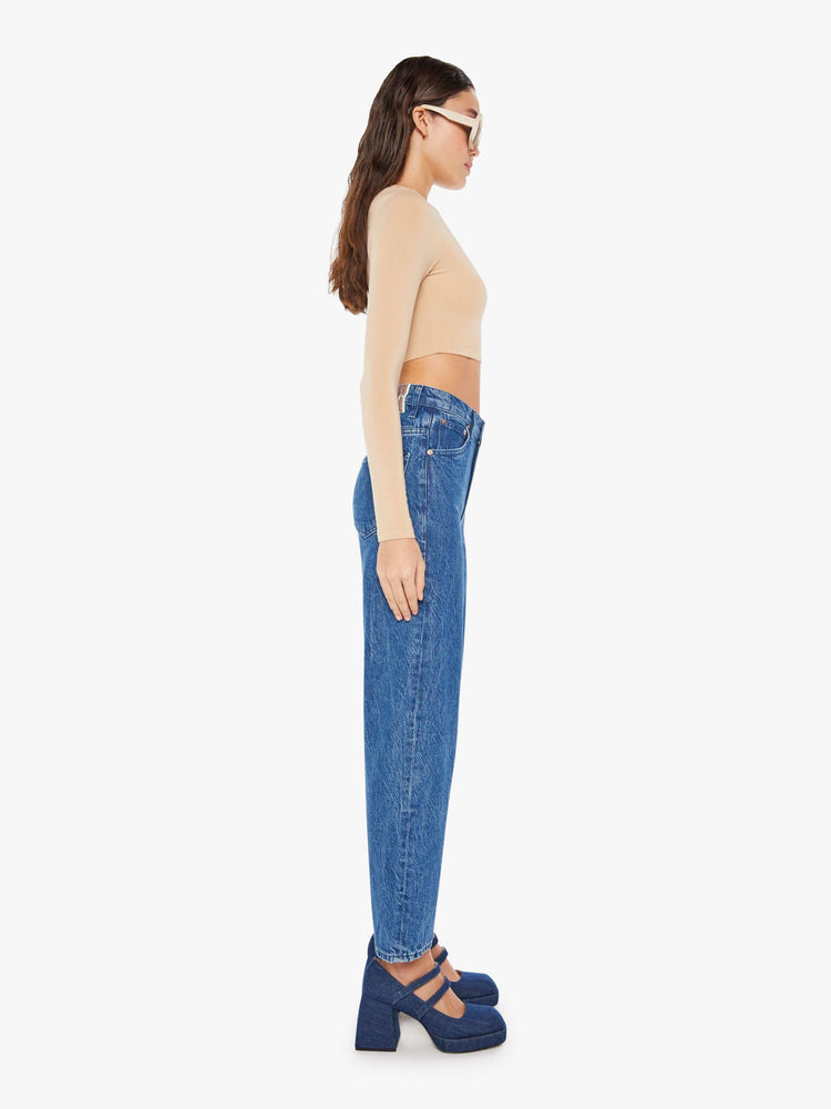 Side view of a womens medium blue wash jean featuring a high rise, straight leg, and a clean ankle length hem.