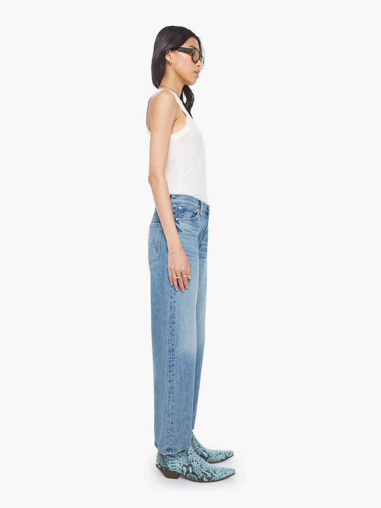 Side view of a woman in a mid blue jeans designed to sit on the hips with a slouchy fit, a loose straight leg, zip fly and a 28.25-inch inseam with a clean hem.