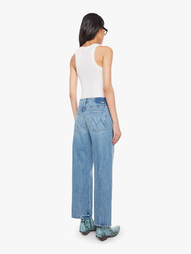 Back view of a woman in a mid blue jeans designed to sit on the hips with a slouchy fit, a loose straight leg, zip fly and a 28.25-inch inseam with a clean hem.