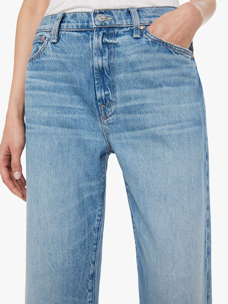 Close up waist view of a woman in a mid blue jeans designed to sit on the hips with a slouchy fit, a loose straight leg, zip fly and a 28.25-inch inseam with a clean hem.