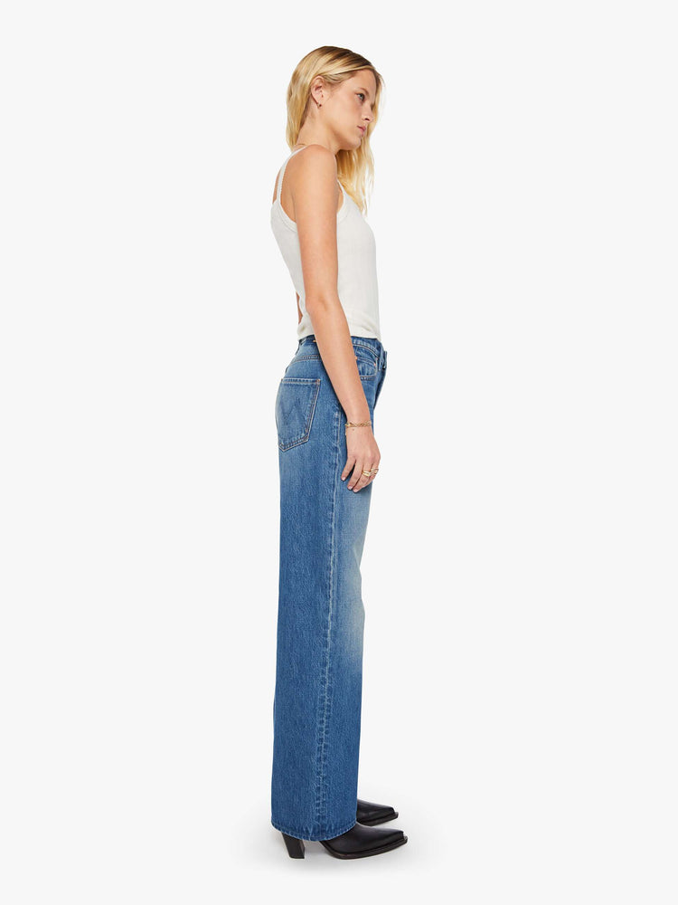 Side view of a woman in a med blue jeans designed to sit on the hips with a slouchy fit, a loose straight leg, button fly and a 28.25-inch inseam with a clean hem.