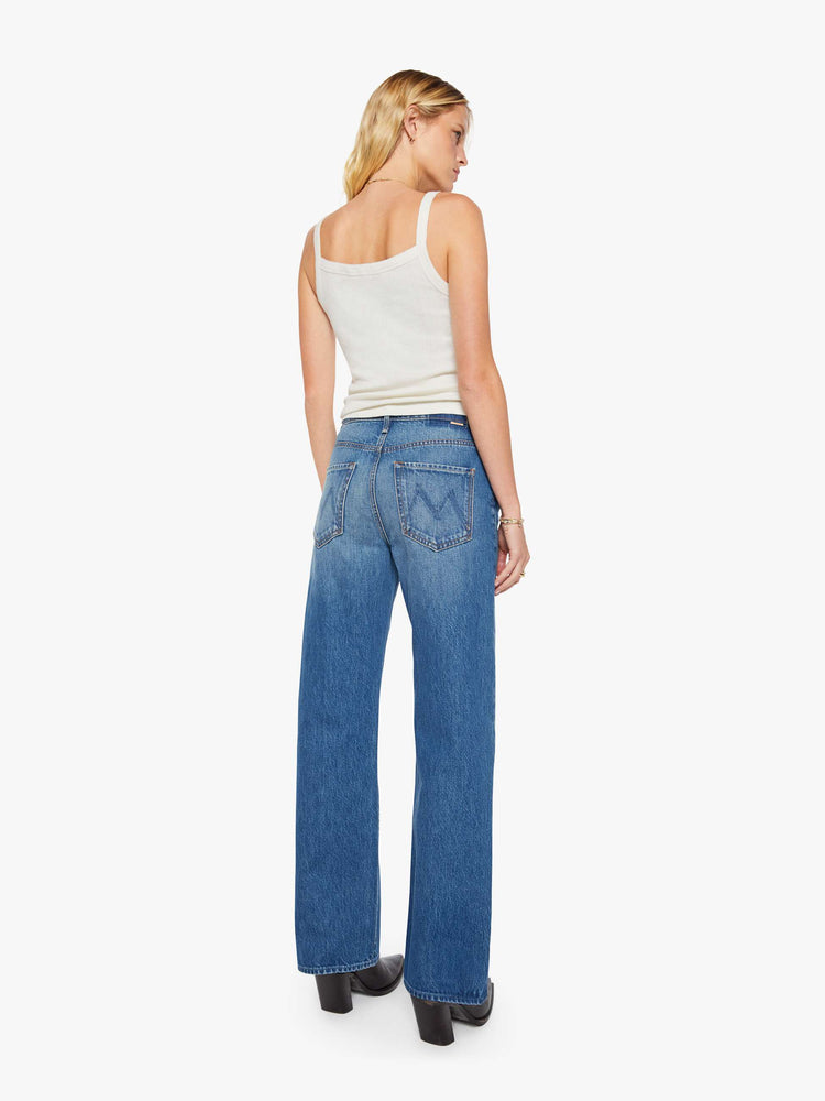 Back view of a woman in a med blue jeans designed to sit on the hips with a slouchy fit, a loose straight leg, button fly and a 28.25-inch inseam with a clean hem.