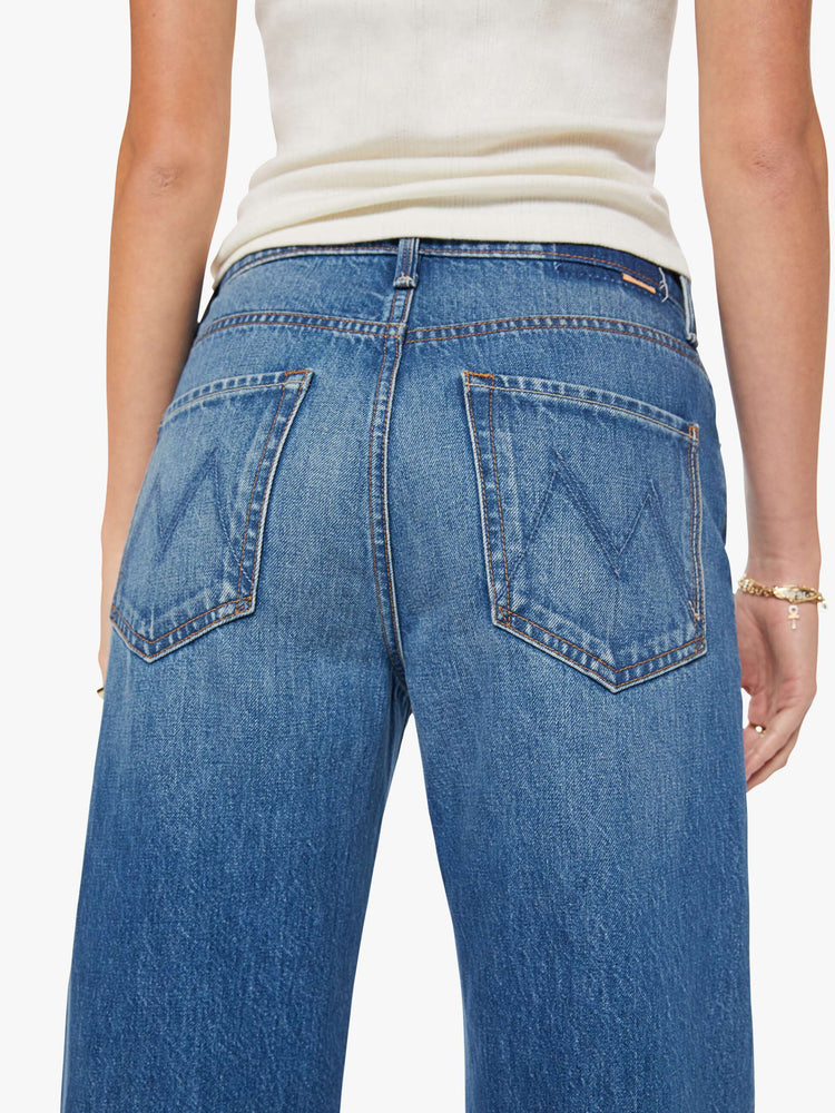 Close up view of a woman in a med blue jeans designed to sit on the hips with a slouchy fit, a loose straight leg, button fly and a 28.25-inch inseam with a clean hem.