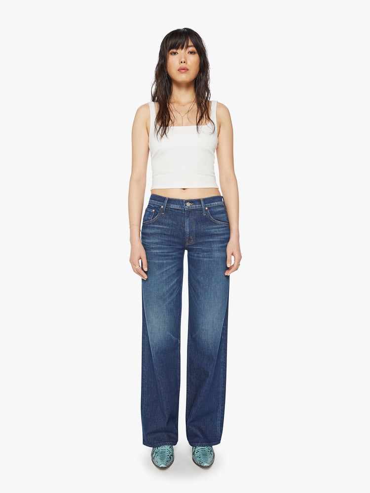 Full body view of a woman low-rise jeans with a loose wide leg, button fly and a long 34-inch inseam with a clean hem in a dark blue wash.