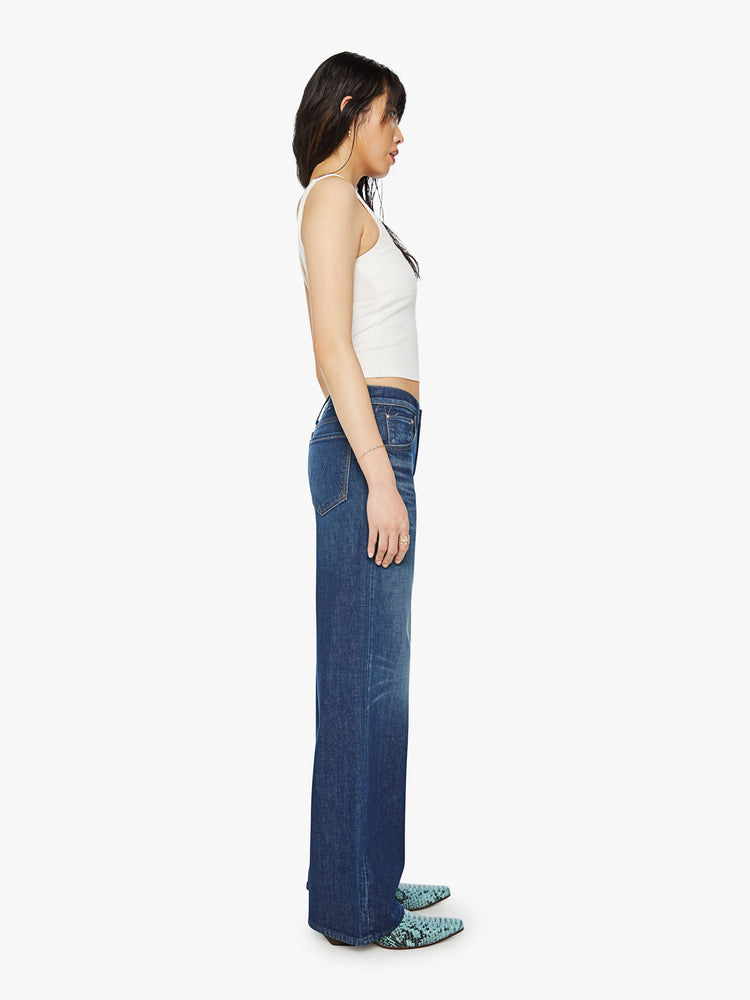 Side body view of a woman low-rise jeans with a loose wide leg, button fly and a long 34-inch inseam with a clean hem in a dark blue wash.