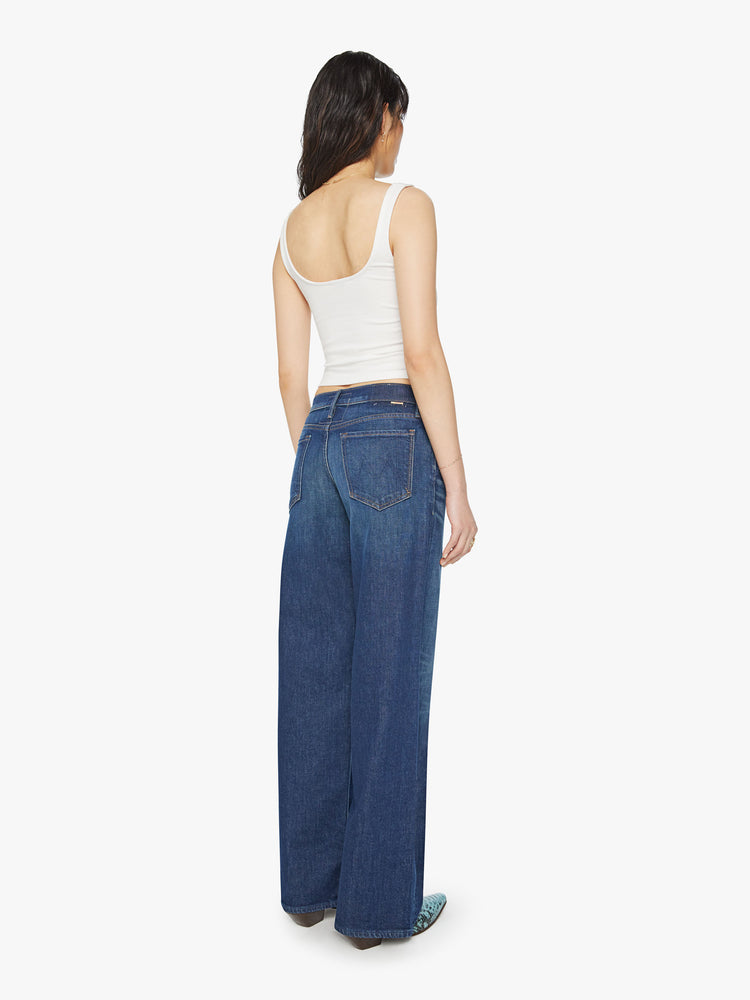 Back body view of a woman low-rise jeans with a loose wide leg, button fly and a long 34-inch inseam with a clean hem in a dark blue wash.