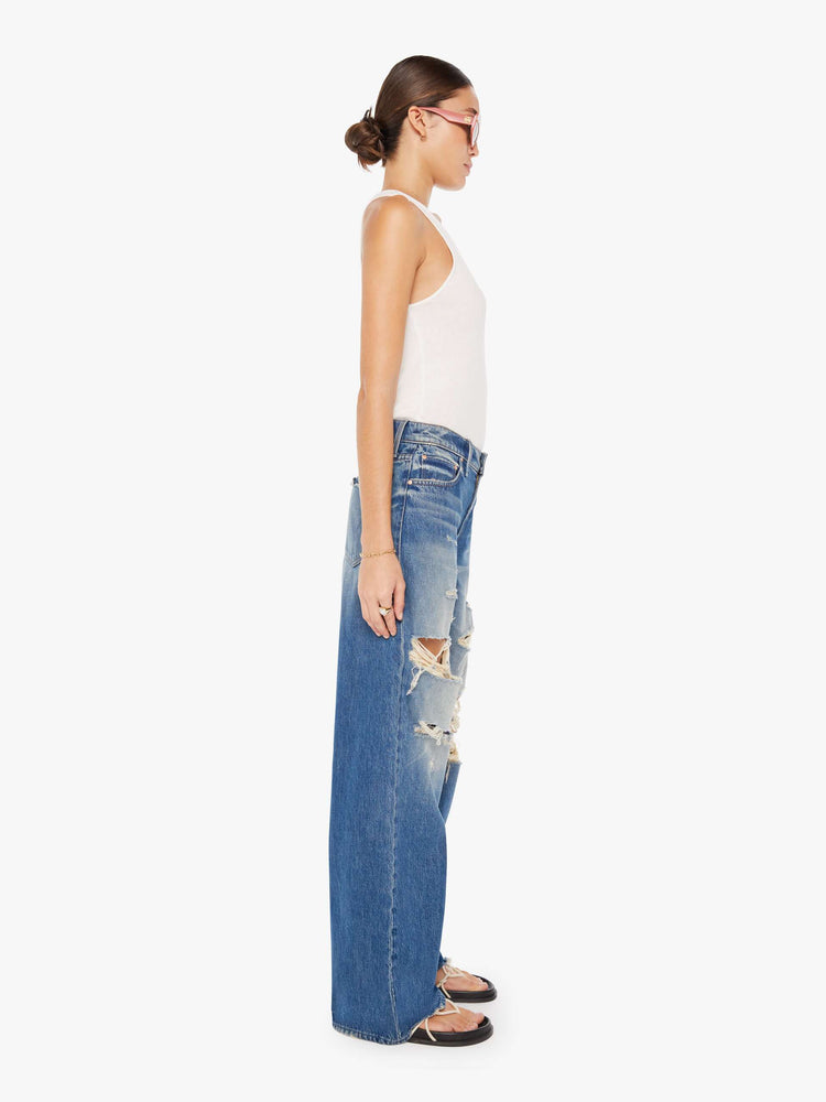 Side view of a womens medium blue wash jean featuring a low rise, wide leg, and distressed details throughout.