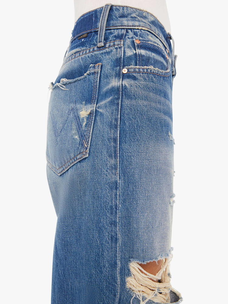 Side close up view of a womens medium blue wash jean featuring a low rise, wide leg, and distressed details throughout.