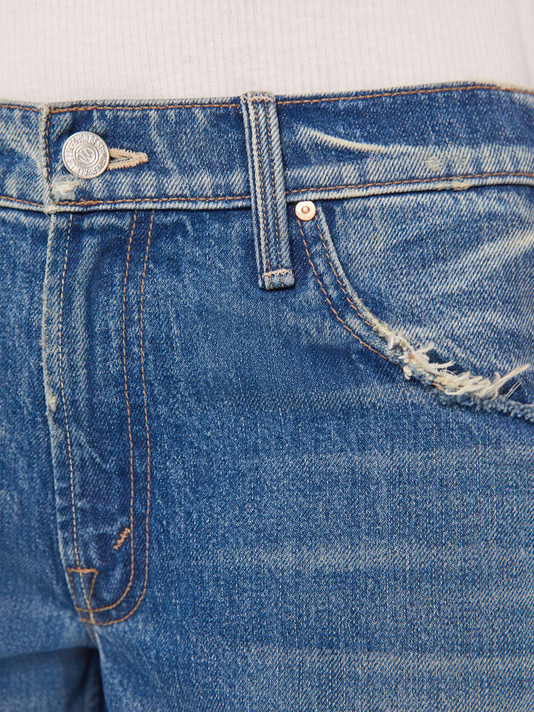 Close up swatch detail view of a medium blue wash jean with distressed details.