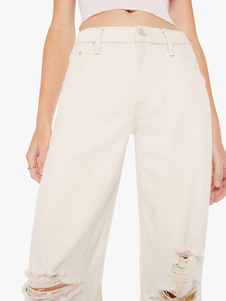 Front close up view of a woman wearing an off white jean featuring a relaxed low rise, a wide straight leg, and distressed knees.
