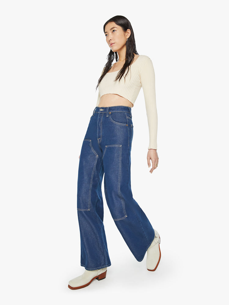 Walking view of a woman super high-rise jeans are designed with a button fly, slouchy, loose fit, panels at the knee and a 31-inch inseam with a clean hem in a wide leg dark blue wash.