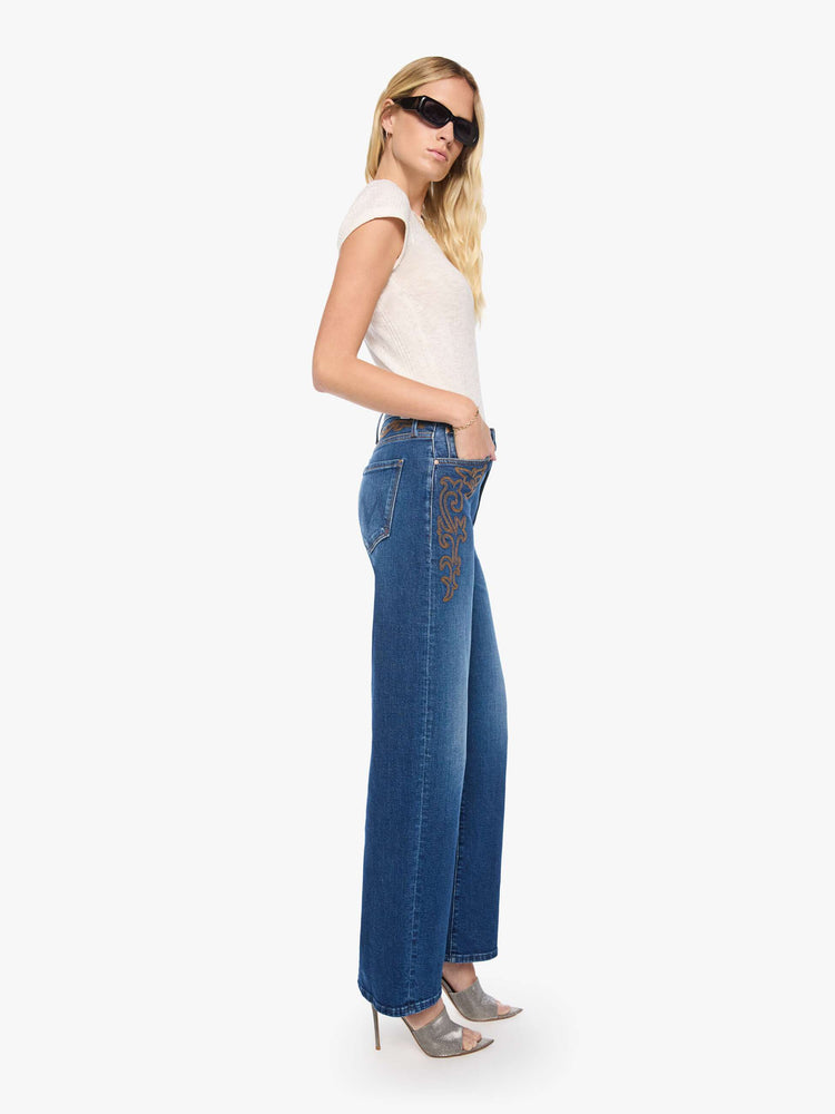 Side view of a woman in a med blue jeans designed to sit on the hips with a zip fly, slouchy fit, loose straight leg and a 32-inch inseam with a clean hem.